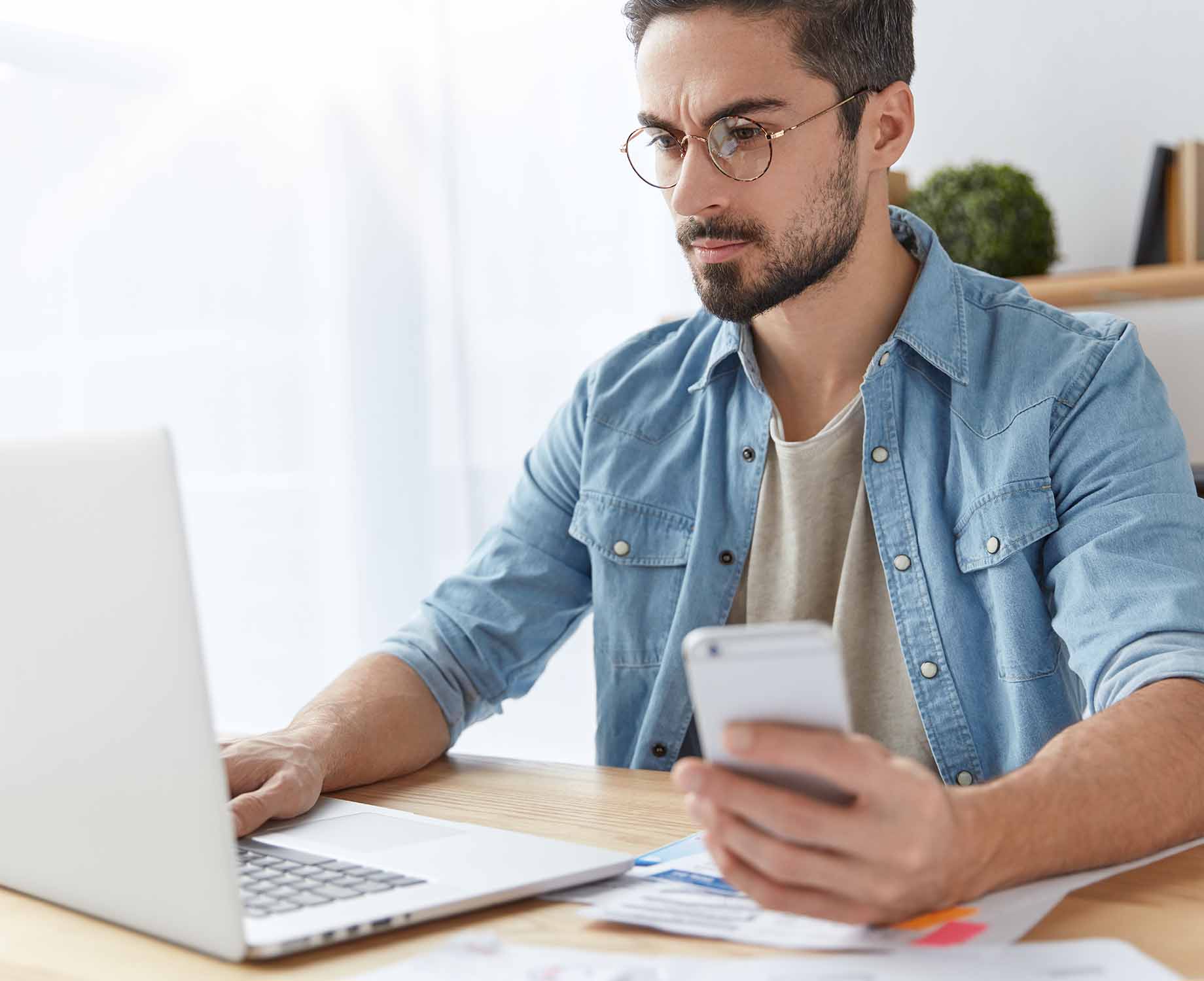 Mann mit Blaulichtfilterbrille Junger Mann von dem Laptop mit Handy in der Hand und Brille